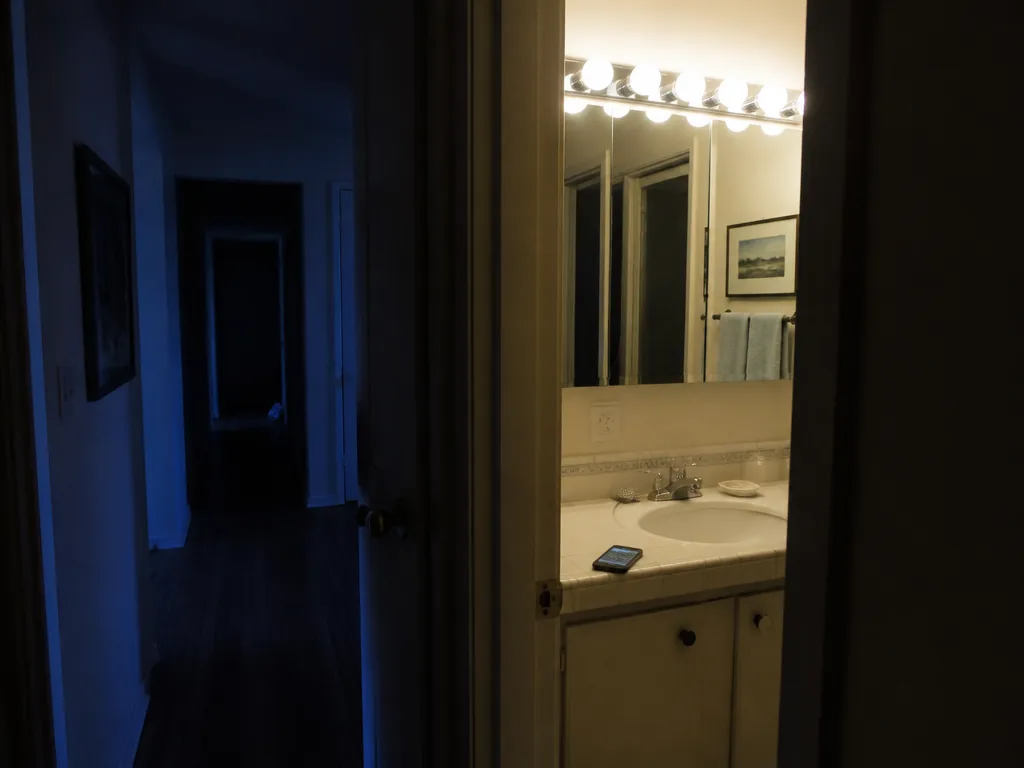 A photorealistic interior photograph taken at night in a small residential bathroom, shot from…