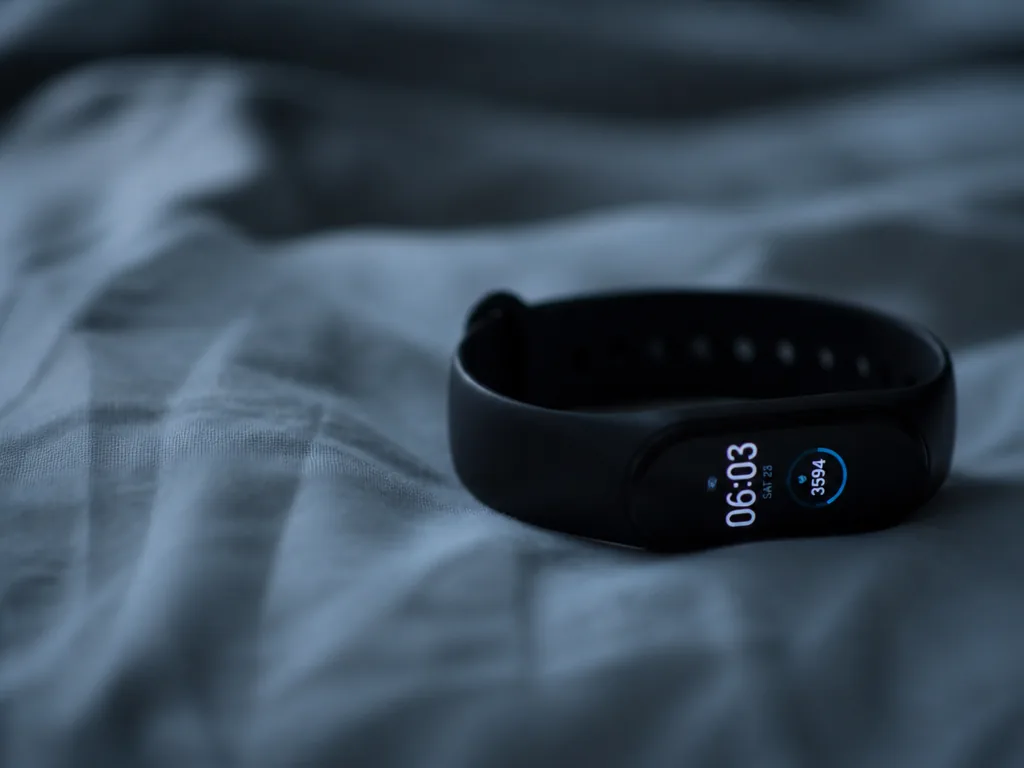 A macro photograph of a slim black fitness tracker band resting on rumpled white…